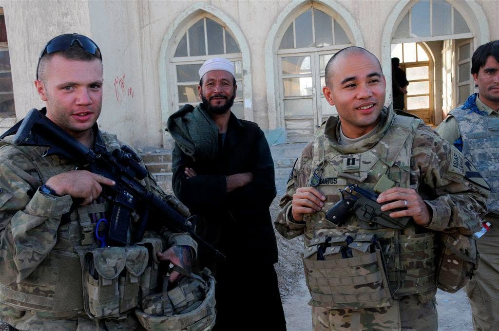 Captain Santos in uniform outside a village building in Afghanistan, alongside another soldier and a local elder